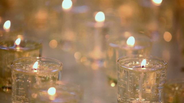 Rows of many candles burn in glasses, closeup view in dark