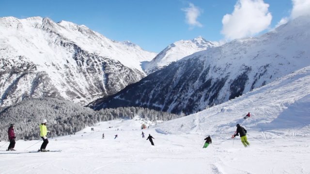 Skiers go on mountain slope downwards against blue sky