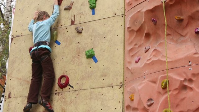 Boy-beginner tries to climb up at rock-climbing wall