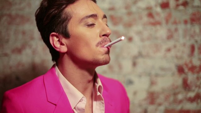 Young man in pink suit with cigarette against scuffed brick wall