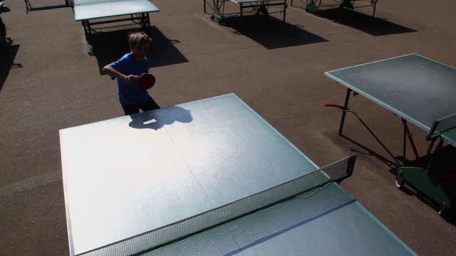 Young boy plays tabletennis at sunny day, view from above