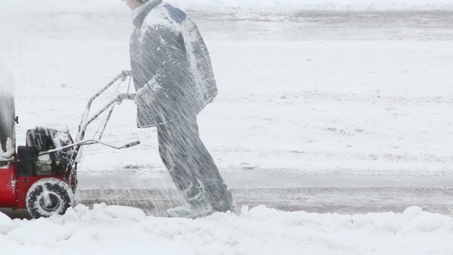 Worker removes snow at footpath with hand snowblower 