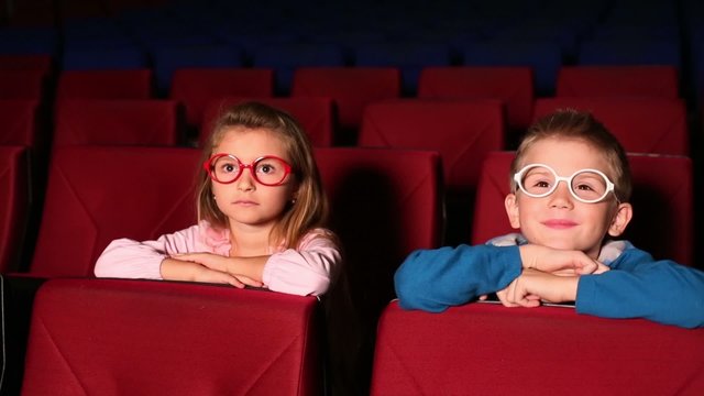Little girl and boy watching a movie at the cinema 