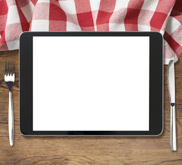 black tablet pc on wooden table with fork and knife