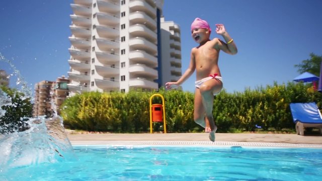 Two little girls run and jump into the pool near the hotel