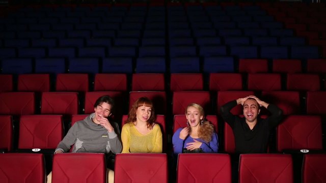 Four people in dark hall cinema watching the film and laugh