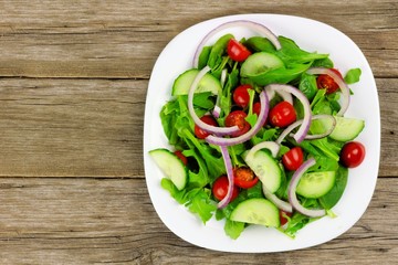 Salad with greens, tomatoes, red onions and cucumber on wood