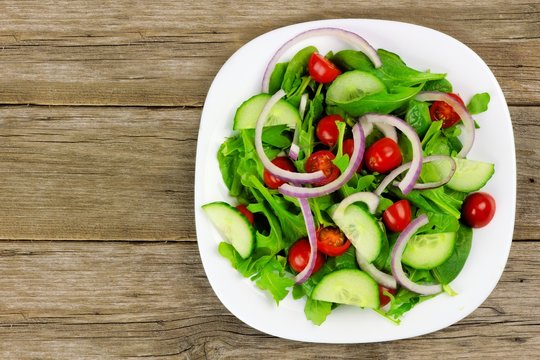 Salad With Greens, Tomatoes, Red Onions And Cucumber On Wood