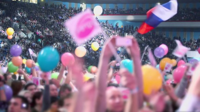 Fans wave flags and sit on tribunes in huge arena during concert