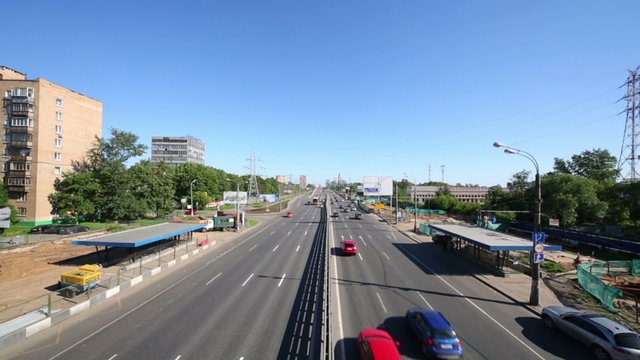Many cars and buses ride by wide road in large city