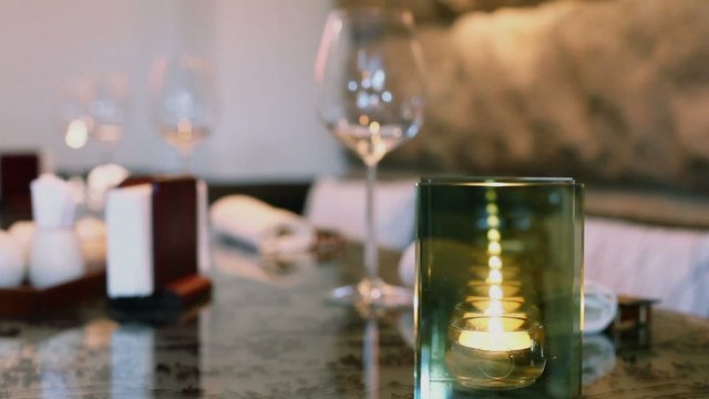 Multiple reflections in candleholder with semi transparent and specular sides which stands on table with glasses at eastern restaurant