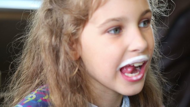 Little girl with milk mustache eats french fries in cafe