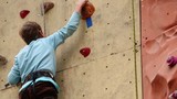 Boy-beginner tries to climb up on vertical rock-climbing wall