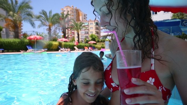 Mother and her daughter sit on underwater chair in bar in pool