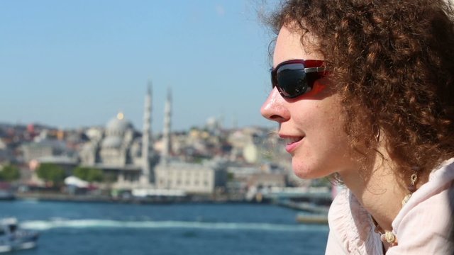 woman in sunglasses looks at landscape with sea shore and mosque