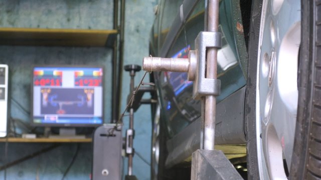 Mechanic tests wheel alignment camber of car on computer in car-care center, time lapse