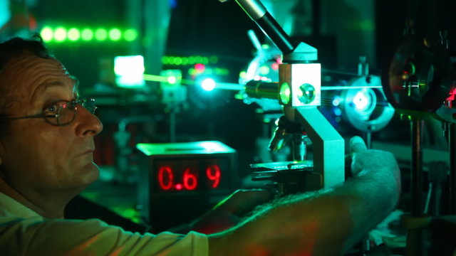 scientist twists handles of control of microscope and on electronic board figures flash