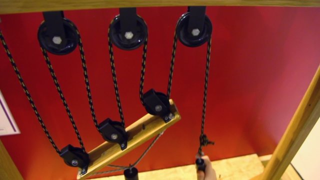 Hand pulls rope with pulleys and cylinder on wooden plate