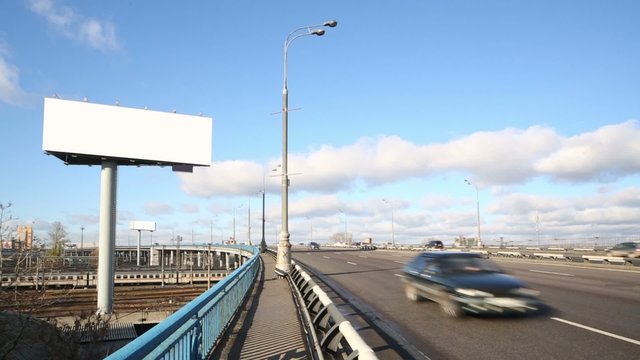 Road with moving cars and large blank billboard at sunny day