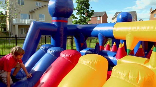 Little boy plays on inflatable playground near cottage at summer day