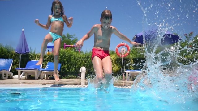 Three children run and jump into the pool near the hotel