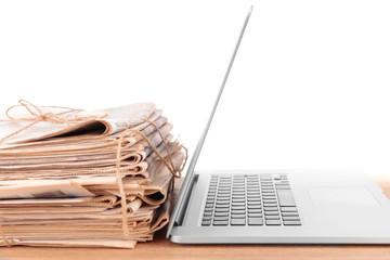 Laptop with stack of newspapers on table isolated on white
