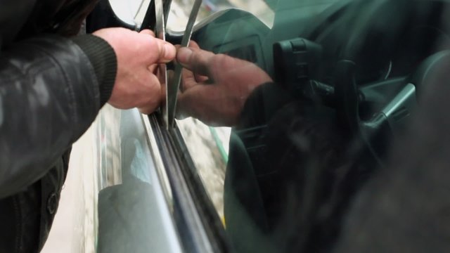 Man in leather jacket tries to break door lock of car
