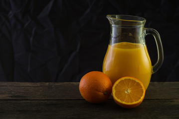 Jug with fresh orange juice, still life art on dark background