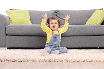 Playful baby girl gesturing happiness seated on floor