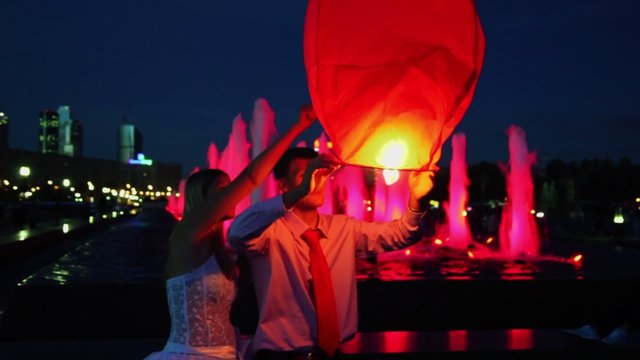 Newlyweds hold japanese lantern near illuminated fountain