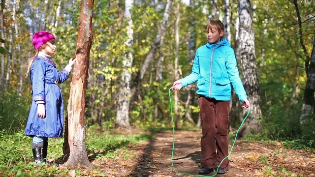 Two children walk in the forest, boy jumping rope.