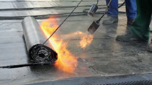 Workers use burners to roll up ruberoid for waterproofing