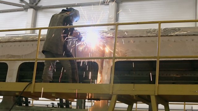 Worker stands on scaffold and weld train wagon
