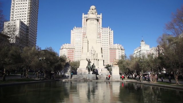 People walk by street and monument to Cervantes at Espana Plaza
