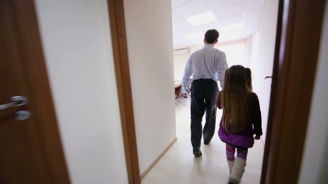 A man walks with his daughter down the hall to a conference room
