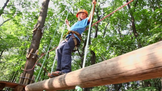 boy in helmet walks by pendant tree log in rope park