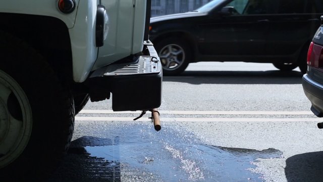 Water drips from under street washing truck which stands at road