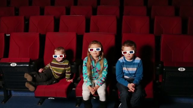 Three children in 3D glasses sit and watching a movie