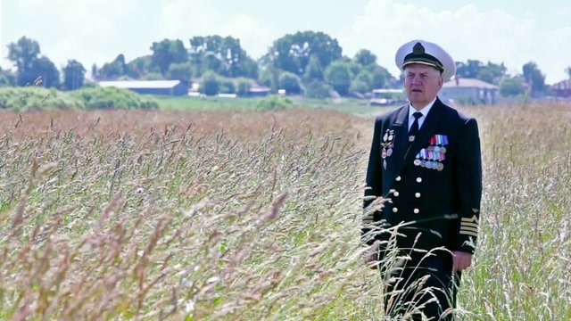 Old man in marine uniform stands among grass in field
