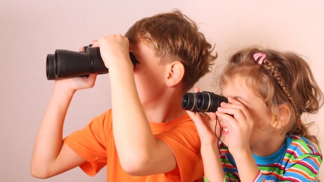 Cute little girl and boy looking through binoculars isolated on white