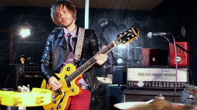Young man plays on guitar in studio with mirror wall