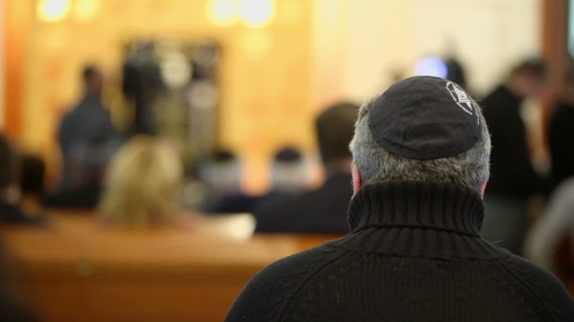 Man in jewish cap sit on bench in synagogue, view from behind