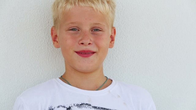 Smiling boy with blond hair open eyes near the wall