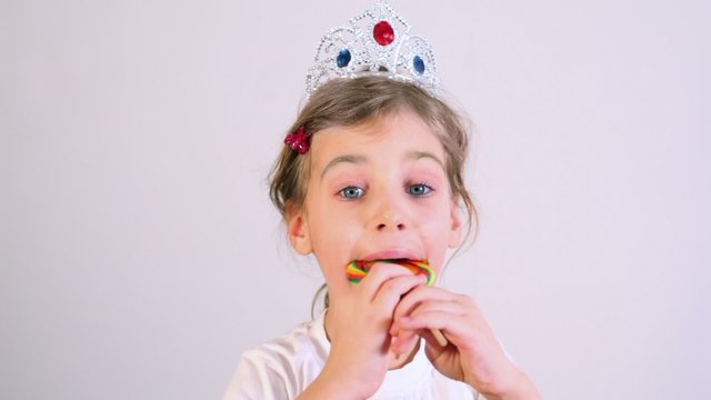 Little girl eats colorful candy with crown on head