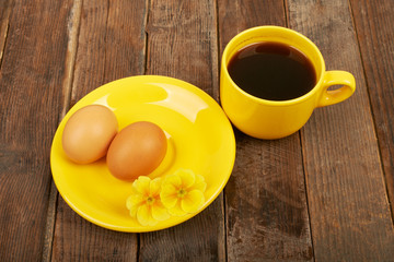 A cup of coffee, flower and eggs on a wooden table background