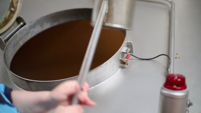 Woman opens hatch and scoops some barm by ladle from big cistern