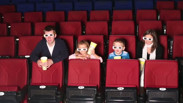 Parents with son and daughter watching film and eating popcorn