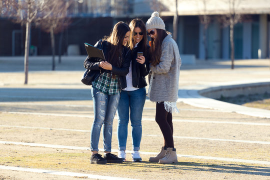 Three students girls using mobile phone in the campus.