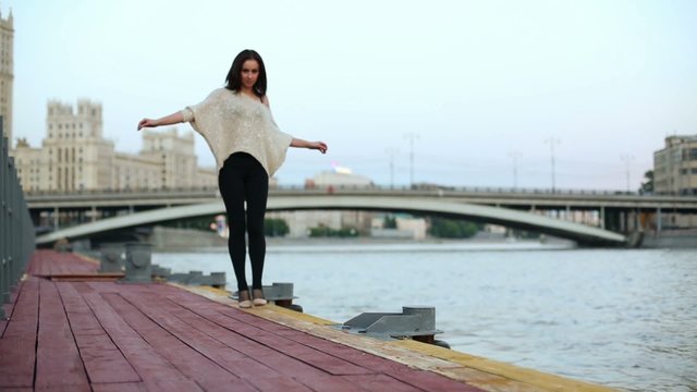 woman walk line on tiptoe along wooden waterfront near railings