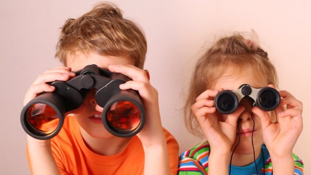 Cute little boy and girl looking through binoculars isolated on white